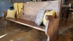 a wooden bench with several pillows on it in a room filled with chairs and tables