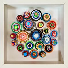 a white frame holds an art work made out of rolled up paper and colored circles