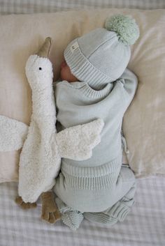 a baby is sleeping on a bed with a stuffed animal and a pillow in the shape of a bird