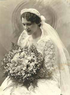 an old photo of a woman in a wedding dress and veil holding a bouquet of flowers