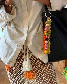 a woman wearing a white shirt holding a black bag and colorful beaded necklaces