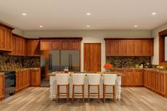 a large kitchen with wooden cabinets and white stools in front of the counter top