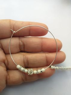 a hand holding a silver hoop with white beads