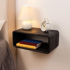 a night stand with books and an alarm clock on the wall next to a bed