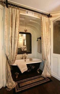 a bath tub sitting under a bathroom mirror next to a window with curtains on it