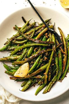 a white plate topped with green beans covered in seasoning next to lemon wedges