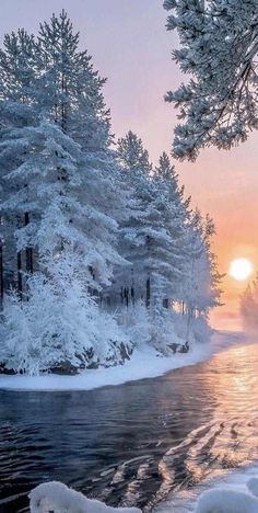 the sun is setting over a snowy river in the middle of some snow covered trees