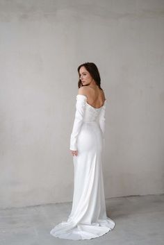 a woman in a white dress is standing against a wall and looking off to the side