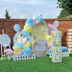 a bunch of balloons and decorations on the grass in front of a brick wall at a baby shower