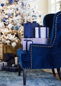 a christmas tree is decorated with blue and white presents in front of a large chair