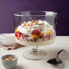 a dessert with fruit and nuts in a glass dish on a table next to a spoon