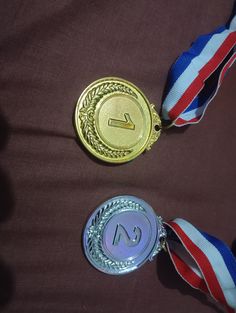 two medals with ribbons around them on a brown cloth covered surface, one is gold and the other is silver