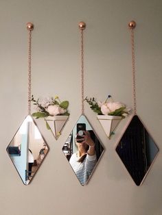 three mirrors hanging on the wall with flowers in them and one is holding a cell phone