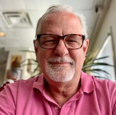 an older man with glasses and a pink shirt is looking at the camera while smiling