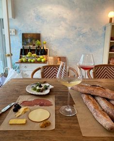 a wooden table topped with cheese and breadsticks next to a glass of wine