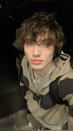 a young man with curly hair wearing a hoodie and looking at the camera while sitting in a car