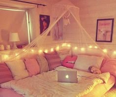 a laptop computer sitting on top of a bed covered in pink and white pillows with lights