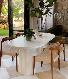 a dining room table with chairs and a potted plant on the center piece, in front of a large glass door