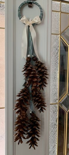 pine cone wreath hanging on the front door with white ribbon and bell ornament