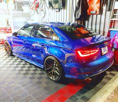 a blue car is parked in front of a garage with red and white checkered flooring