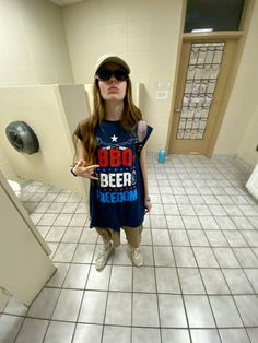 a woman standing in a restroom wearing sunglasses and a t - shirt that says bbq beer