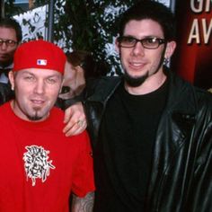 two men standing next to each other in front of a red carpeted area with people