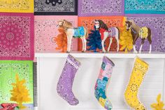 colorful christmas stockings hung on a fireplace mantel in front of brightly colored paper cut - outs