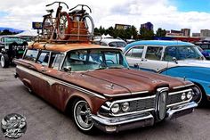 an old station wagon is parked in a parking lot with other cars and bicycles on top