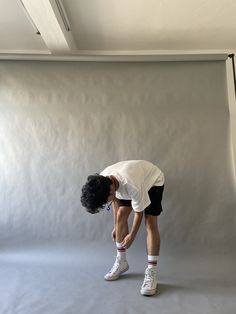 a man in white shirt and black shorts bending over with tennis shoes on his feet