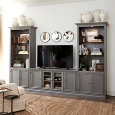 a living room with gray entertainment center and white vases on the wall above it