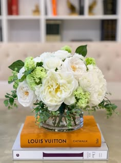 a bouquet of white flowers in a glass vase on top of a stack of books