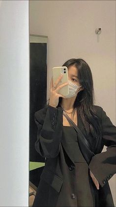 a woman taking a selfie in front of a mirror wearing a face mask and black blazer