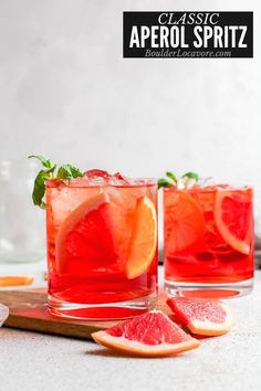 two glasses filled with red liquid and garnished with grapefruit, orange slices and mint