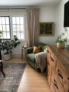 a living room filled with furniture next to a window and a wooden dresser in front of a large window