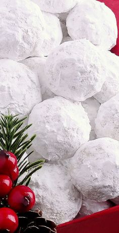 a red box filled with snowball cookies next to pine cones and holly wreaths