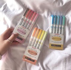 four different colored pens are on the bed and someone is holding them in their hand