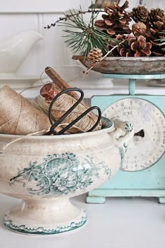 a white bowl filled with twine and pine cones on top of a table next to a scale