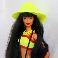 a barbie doll wearing a yellow hat and holding a black handbag on a white background