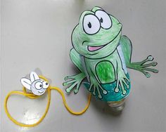 a green frog sitting on top of a light bulb next to a paper cutout