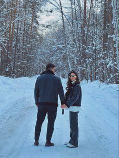 a man and woman holding hands while standing in the middle of a snow covered road