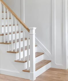 a white staircase with wooden handrails and wood flooring in an empty room