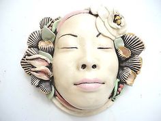 a ceramic head with flowers and leaves on it's face, sitting on a white surface