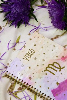 an open notebook sitting on top of a table next to purple flowers