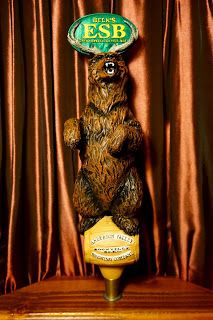 a brown bear holding a beer bottle on top of it's head with an esb sign above its head