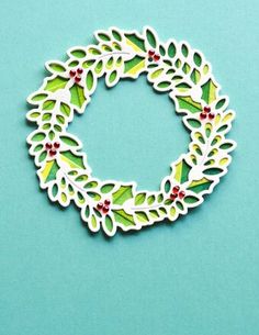 a paper wreath with holly leaves and red berries is on a blue surface, ready to be cut out