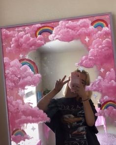 a woman taking a selfie in front of a mirror with pink clouds and rainbows