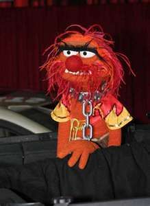 an orange and red stuffed animal with chains on it's neck sitting in front of a car