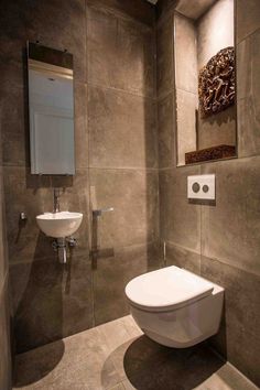 a bathroom with a toilet, sink and mirror in the corner on the tiled wall