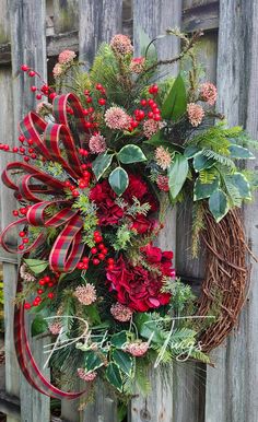 a wreath with red flowers and greenery hanging on a wooden fence