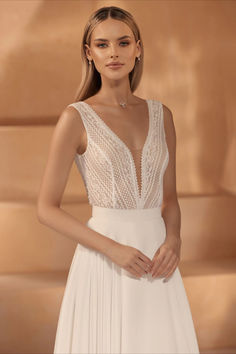 a woman in a white wedding dress standing next to a tan wall with her hands on her hips